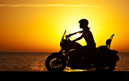 Woman biker over sunset, female riding motorcycle, motorbike driver traveling, girl racing on the beach road, freedom lifestyle