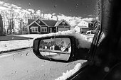 Rear mirror of car covered with snow reflecting a street.