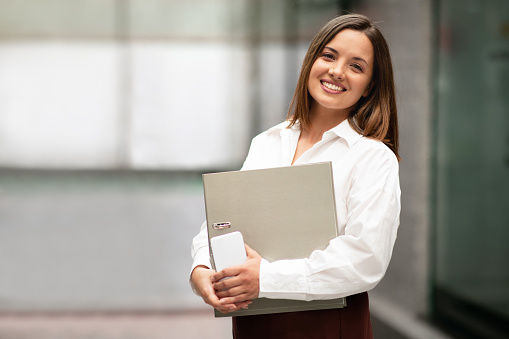 Successful Business Career. Millennial Businesswoman In Formal Wear Holding Folder With Papers And Documents, Smiling To Camera Advertising Job Offer, Standing In Modern Office, Copy Space