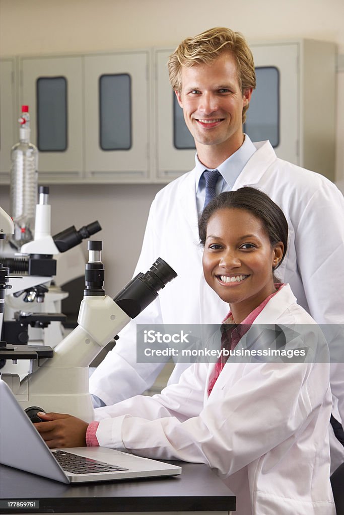 Male And Female Scientists Using Microscopes In Laboratory Male And Female Scientists Using Microscopes In Laboratory Smiling At Camera Laboratory Stock Photo