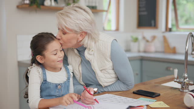 Love, happy and grandmother drawing with her grandchild in the kitchen for creative art at home. Education, bonding and senior woman kissing a child while helping with school homework at family house