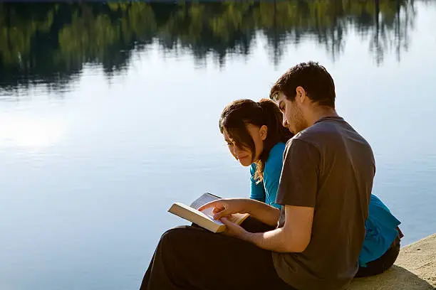 Two young adults sitting by a lake and studying the Bible (King James Version)