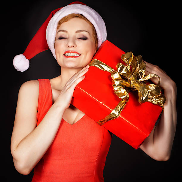 Mature smiling woman wearing santa hat  holding  Christmas gift stock photo