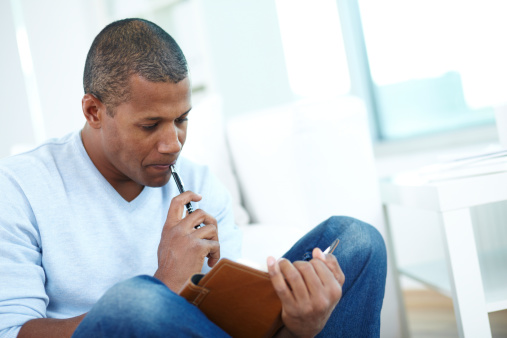 Image of pensive African man with notepad and pen
