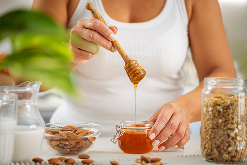 Woman holding honey jar an dipper preparing healthy breakfast