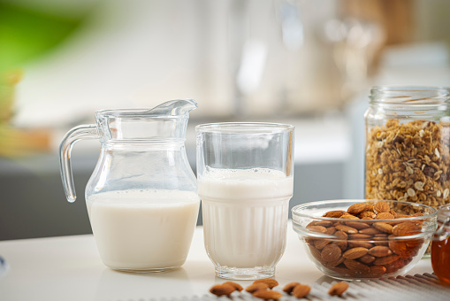 Fresh almond milk and peeled almonds on kitchen counter