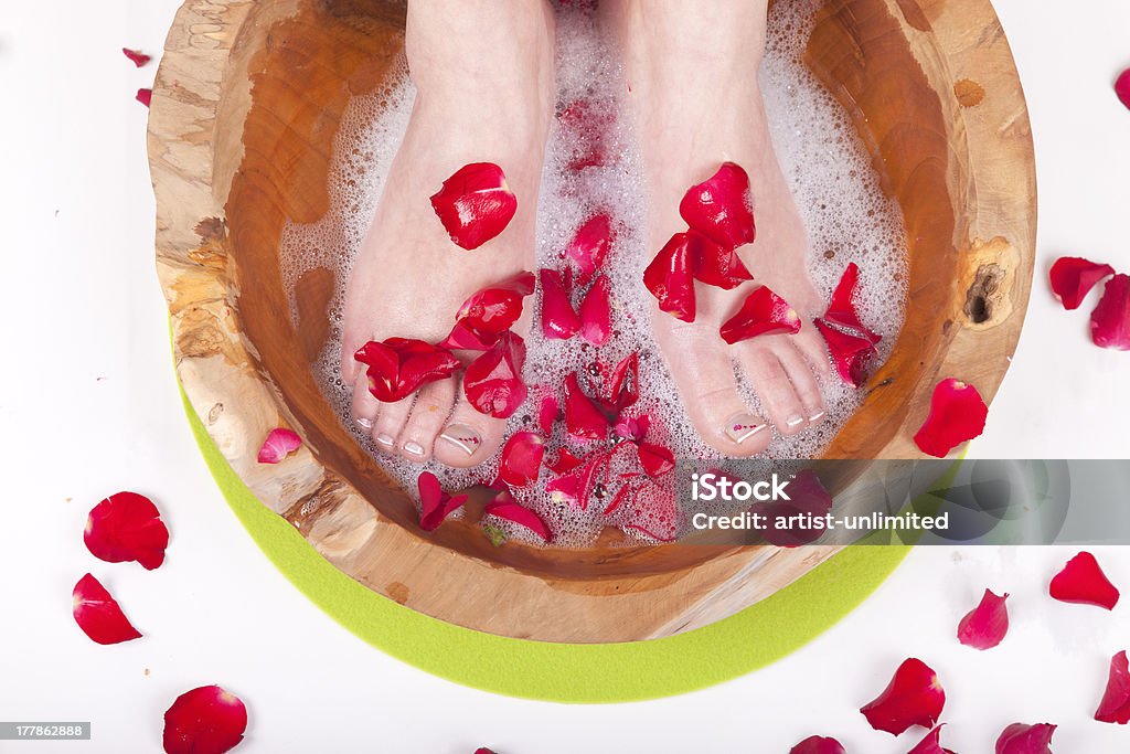 spa foot treatment woman foot pedicure with a wooden bowl, water and red rose petals. Adult Stock Photo