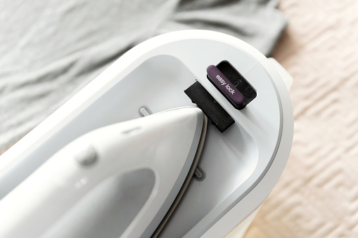 smart steam generator for ironing clothes with ecological mode. housework concept. the modern iron is on the bed.