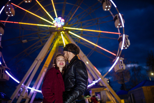 couple in love in an amusement park near a ferris wheel on a date in cold weather. The concept of love and joy in relationships.