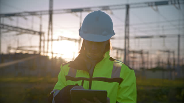 SLO MO Female Electrical Engineer Using Digital Tablet While Walking At Power Station During Sunset