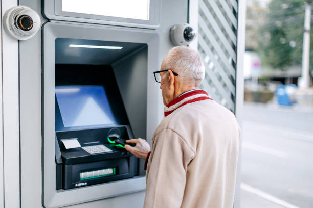 istock Old man picking money using smart phone in front of ATM 1778641420
