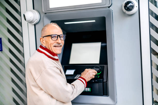 istock Old man picking money using smart phone in front of ATM 1778641966