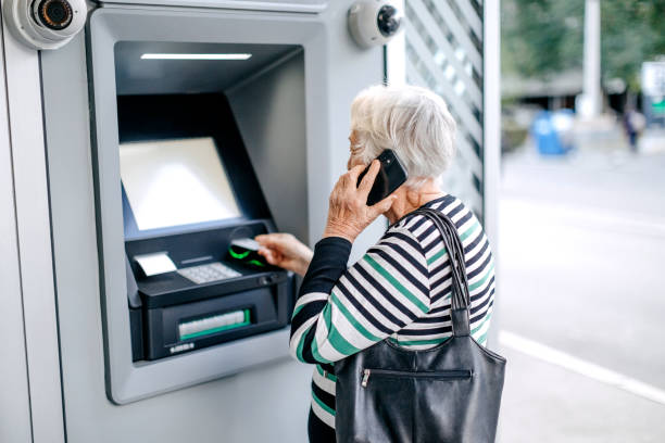 istock Old woman picking money using ATM while talking on mobile phone 1778642334