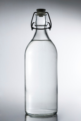 A empty old bottle with a rubber stopper is isolated on a gray background.  The picture has an old sepia and grainy picture effect.  Can be use to symbolize starting out, future, empty, etc.   Empty space for text.