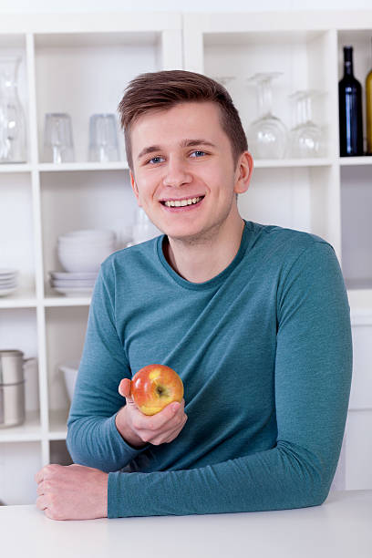 istock young man eating an healthy apple in his kitchen 177866395