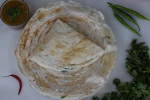 Crisp carrot onion dosa. A ghee roast dosa made with fermented batter of rice and lentils added with grated carrots, chopped onions and coriander leaves to the batter. Served with a bowl of sambar.