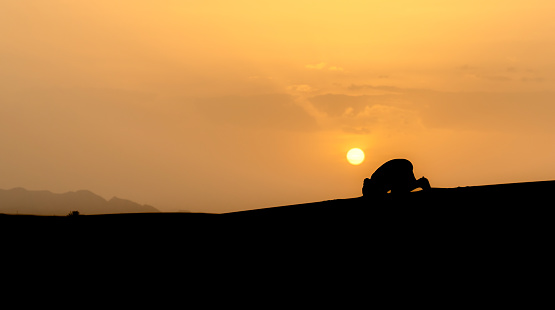 Silhouette of unidentified muslim Berber man praying in Sahara Desert, Morocco