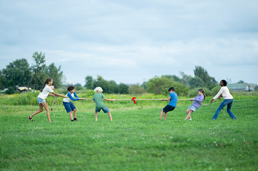 A small group of school aged children pull a rope with all their might, as they participate in a game of tug-of-war.  They are each dressed casually and are smiling and laughing as they pull together.