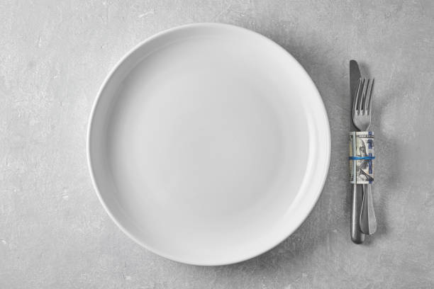istock An empty white plate and a dinner fork and knife wrapped in a hundred dollar bill. Tips to the waiter in a restaurant 1778676693