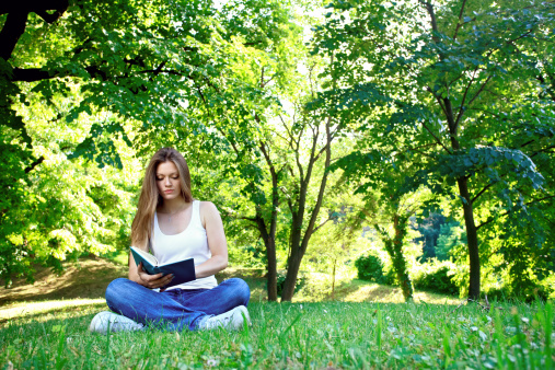 Young woman sitting in park and reading book