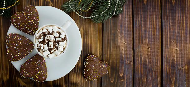 Hot chocolate with marshmallows in the white cup and heart shaped Christmas cookies on the wooden background. Top view. Copy space.