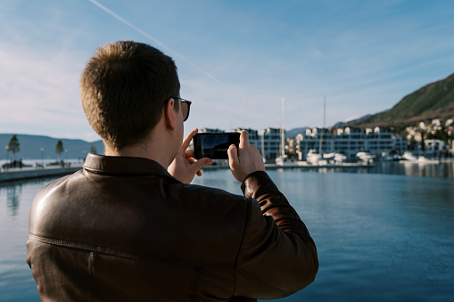 Man takes pictures of high-rise buildings on the seashore with a smartphone. Back view. High quality photo