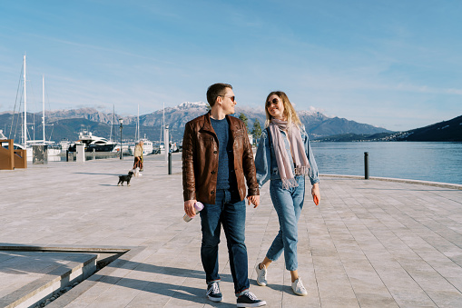 Man and woman walk holding hands and looking at each other along the pier by the sea. High quality photo