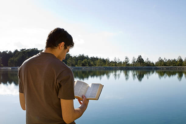 hombre leyendo libro junto al lago - kjv fotografías e imágenes de stock