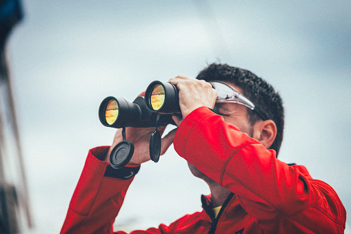 Sailor with binoculars on sailboat observing.