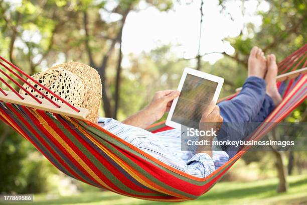 Man Wearing Hat Relaxing In Hammock With Ebook Stock Photo - Download Image Now - Hammock, Reading, Summer