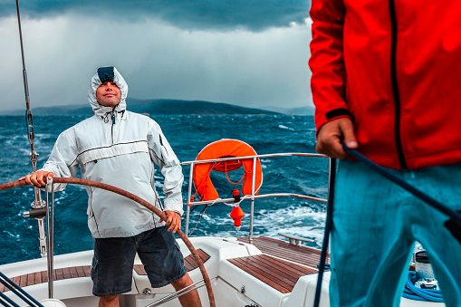 Crew members enjoying sailing on sailboat in hard weather conditions.