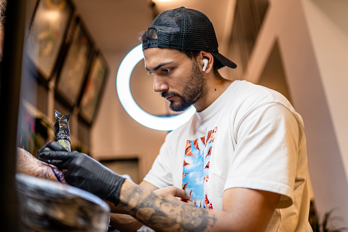 Young tattoo artist tattooing his customer in his studio