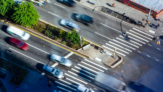 High angle view of a crosswalk in Brooklyn, NYC, with morning commuter traffic on the streets, cars and trucks with motion blur and pedestrians on the sidewalk.