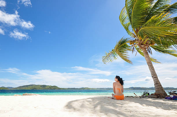 istock young girl sitting on beach under coconut tree 177873409