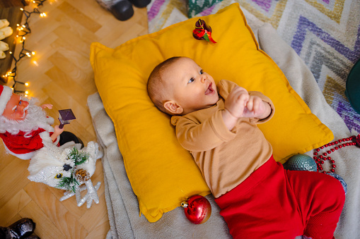 Cute, little baby girl is laying on a big, yellow pillow, placed on the floor.
