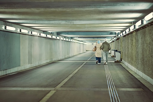 Two people, a man and a woman, walking hand in hand up a long, dimly lit concrete tunnel