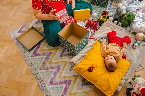 Amidst the Christmas rush, a mother is packing gifts while her baby girl peacefully lays on the floor.