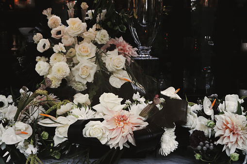 A view inside a flower shop with Fresh Flowers including Dahlias, Roses and Anemone Fresh cascading down Dark Cabinet onto Marble Counter