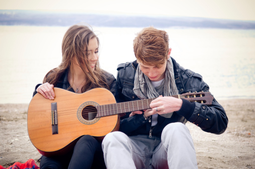 Young girl with acoustic guitar and her boyfriend on the bach