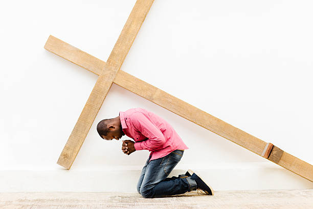 joven cristiano afroamericano postrado arrodillado orando cruz de madera - praying men god kneeling imagens e fotografias de stock