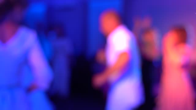 Women and men dancing at a disco in neon light, blurry video.