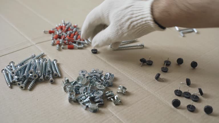 A male worker goes through the furniture fasteners after unpacking, preparing to assemble the furniture.