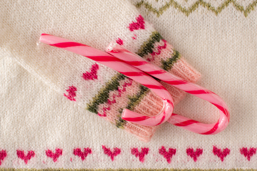 Warm woolen Christmas sweater sleeve with red hearts pattern and candy cane sweets. Close up. Flat lay. Funny Christmas concept.