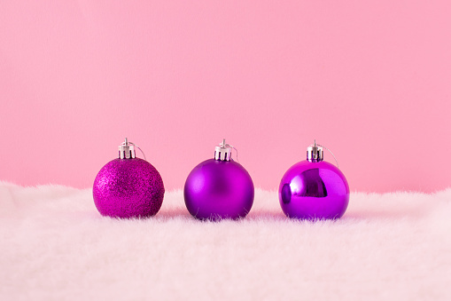 Purple shiny and glittering Christmas ornament balls on a fluffy fur and pastel pink background. Holiday home decoration concept. Christmas aesthetic.