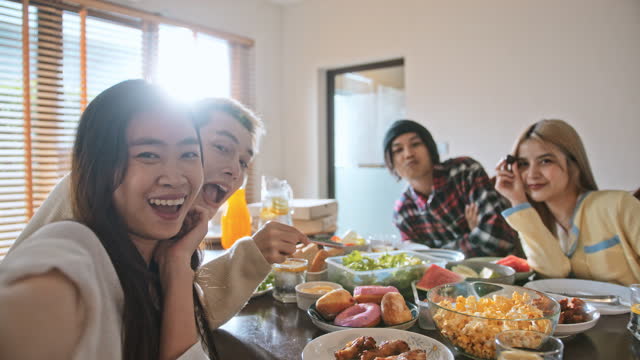 Group of young millennial Asian teenager enjoy party meal at home, brunch or lunch table, friend selfie on mobile phone happy together. Diverse gender with LGBTQ+ people. Fun social meeting concept