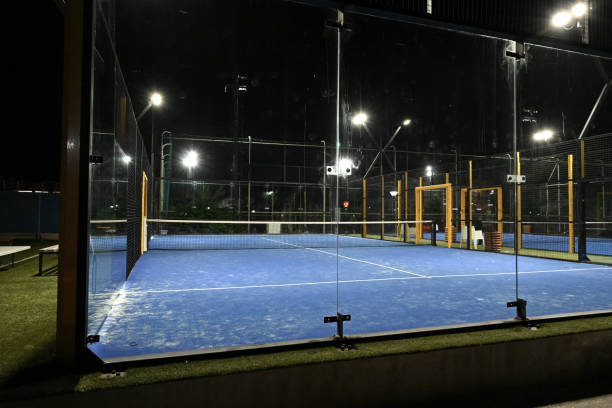 terrain bleu fermé éclairé pour le padel pendant la nuit avec une construction créée par le grillage et les murs arrière en verre. - tennis club photos et images de collection