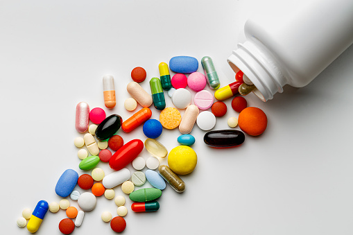 Health themes: Large group of assorted capsules and pills coming out from pill container on a white background