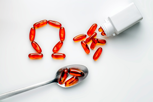 Heath Themes: Close up of fish oil vitamin gelatin capsules with Omega-3 into spoon laying on white background