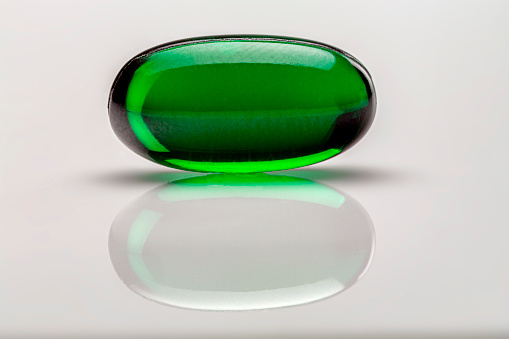 Heath Themes: Close up of single green gelatin capsule on white background