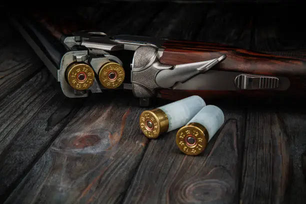 Photo of Classic trigger double-barreled hunting rifle on a wooden background. Smooth-bore hunting rifle open for reloading. Concept postcards for hunters.